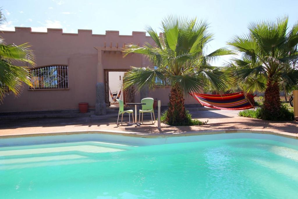 a swimming pool with two chairs and a table and palm trees at Maison d hôtes Bungalow Villa Hammam Bien-être et Piscine in Agadir