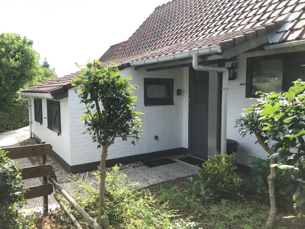 una casa blanca con una puerta y un árbol en Vissershuisjes ‘Duinendaele 65’, en De Panne