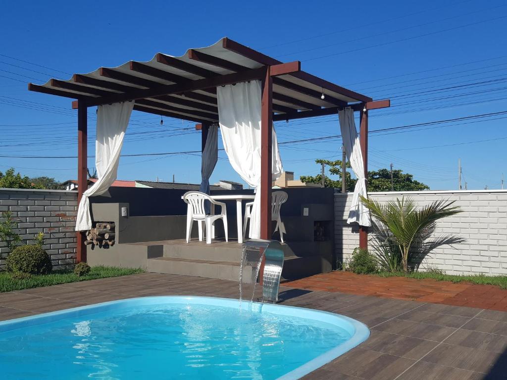 una pérgola sobre una piscina con mesa y sillas en Casa Esquina do Mar, en São Francisco do Sul