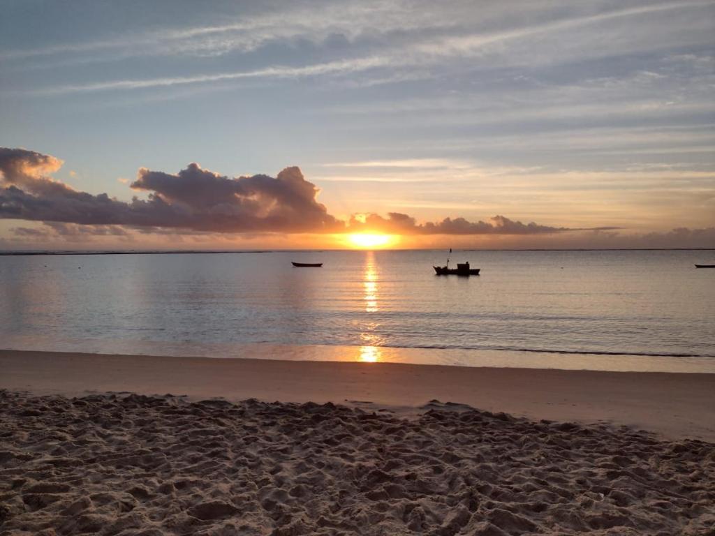 een zonsondergang op het strand met een boot in het water bij Casa de Praia in Coroa Vermelha