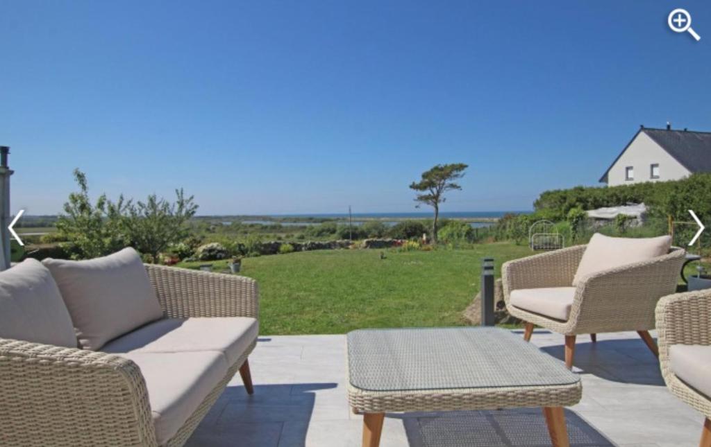 un patio con muebles de mimbre y vistas al océano. en Le Clos de l'Abré en Gatteville-le-Phare