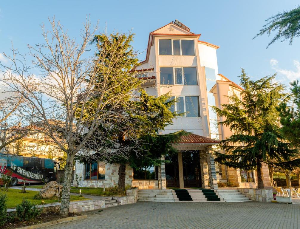 un edificio alto con un árbol delante de él en Hotel George, en Korçë