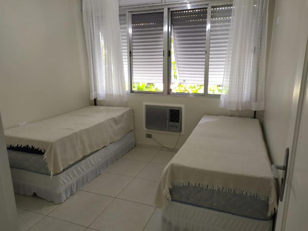 Guarujá Enseada - Apto 200m da praia - 02 dorm. Wi-fi + AR + Estacionamento في غوارويا: غرفة نوم صغيرة بسريرين ونافذة