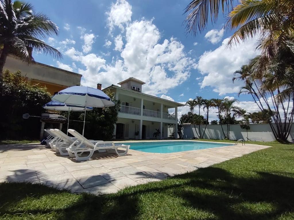 a house with a swimming pool and two chairs and an umbrella at Casa Eventos e Temporada com 4 suites, piscina, churrasqueira, Wi-Fi, Ar Condicionado - Proximo Praia Mar Casado e Pernambuco - Guaruja - in Guarujá