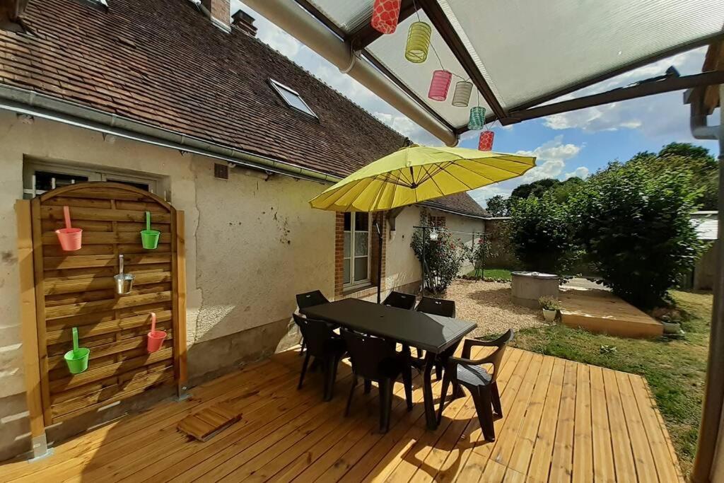 een patio met een tafel en een gele parasol bij Gîte Le temps suspendu à PEZOU 41 in Pezou
