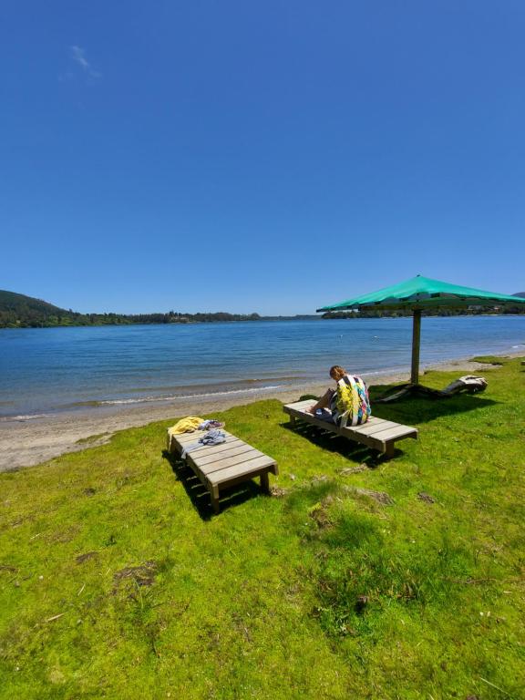 a person sitting under an umbrella on a beach at Complejo Pehuen Lago Lanalhue in Cañete