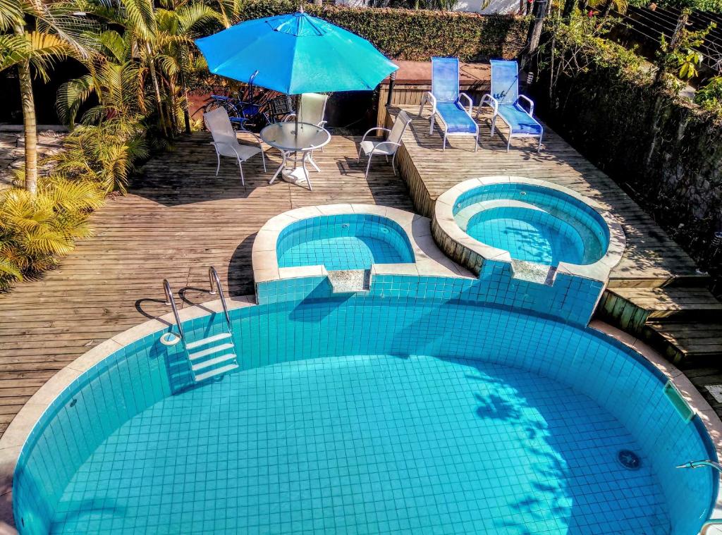 two swimming pools with chairs and an umbrella at Chalés e Flats Refúgio de Camburi in Camburi
