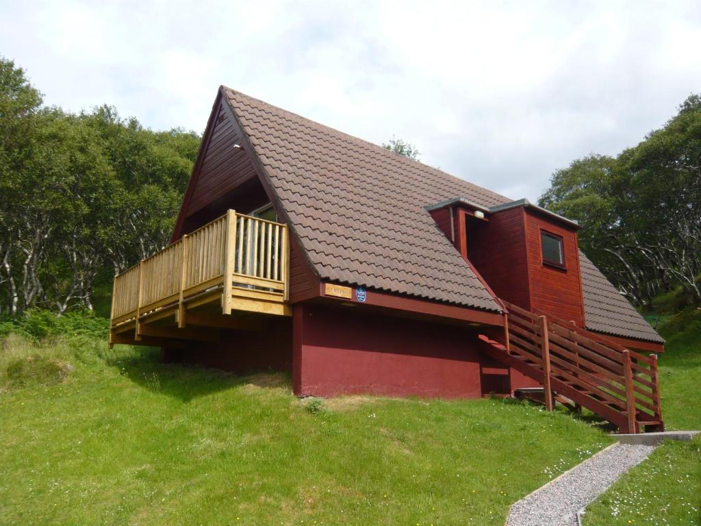 una pequeña casa roja con terraza en una colina en Lochinver Holiday Lodges & Cottages en Lochinver