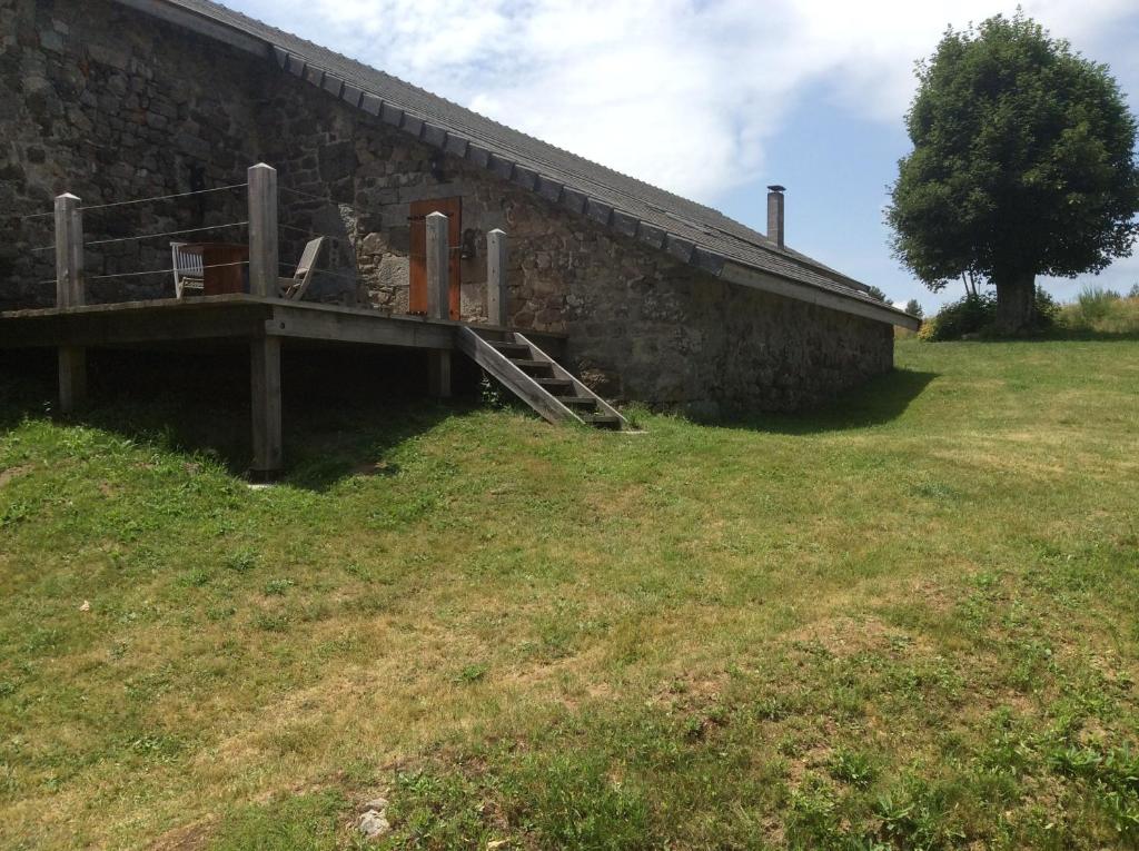 ein Steingebäude mit einem Holzsteg neben einem Feld in der Unterkunft Le Carré gourmand in Le Chambon-sur-Lignon