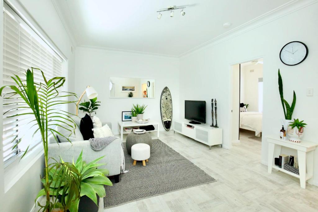 Beautifully renovated quiet unit in Cronulla في كرونولا: غرفة معيشة بيضاء مع أريكة وتلفزيون