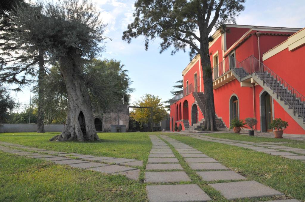 a red building with a tree next to a sidewalk at Palazzo Rosso in Riposto