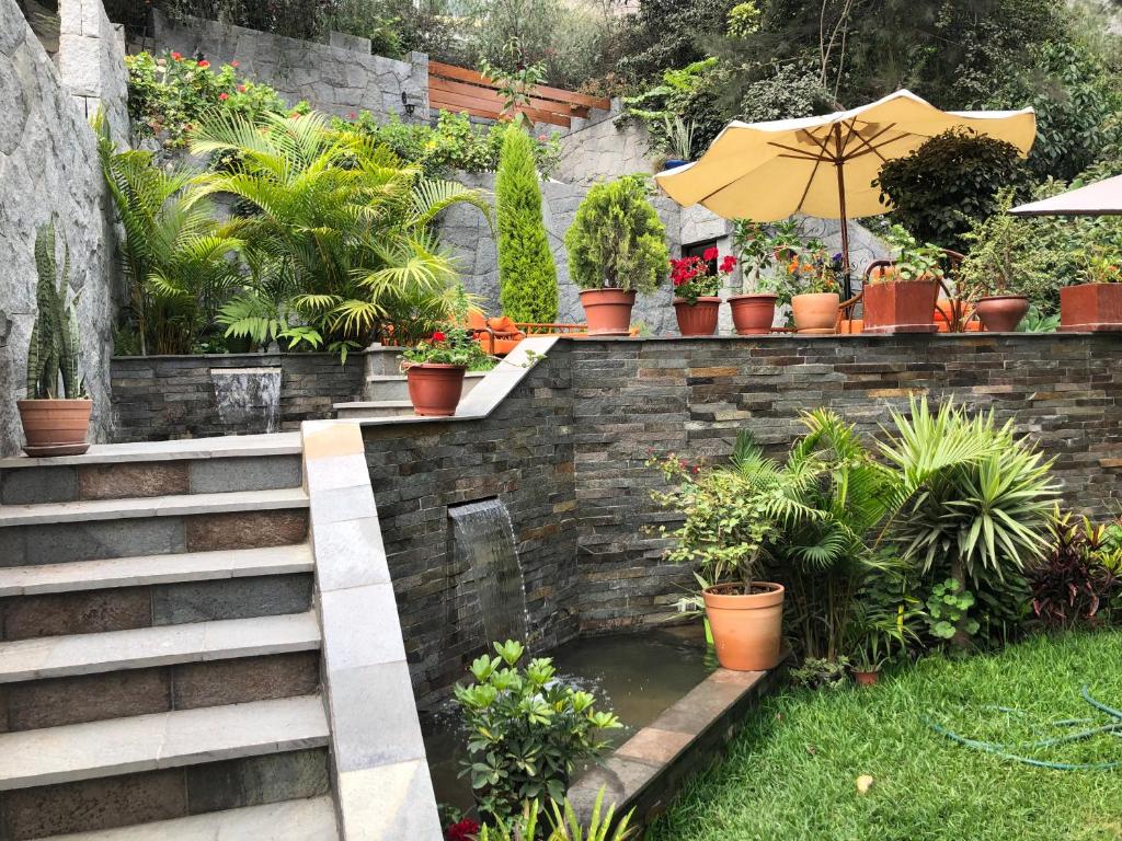 einen Garten mit einem Teich mit Topfpflanzen und einem Sonnenschirm in der Unterkunft Casa Campo Machu Picchu - Club Los Girasoles, Chaclacayo in Chaclacayo