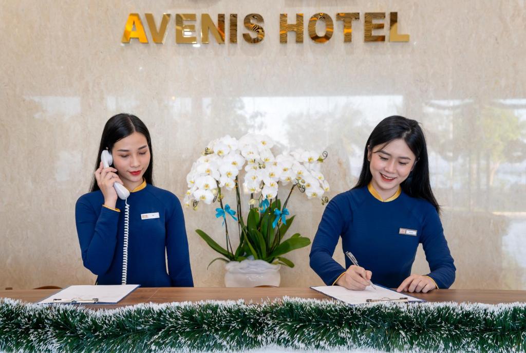 twee vrouwen die aan een tafel zitten te praten op mobiele telefoons bij Avenis Hotel in Da Nang