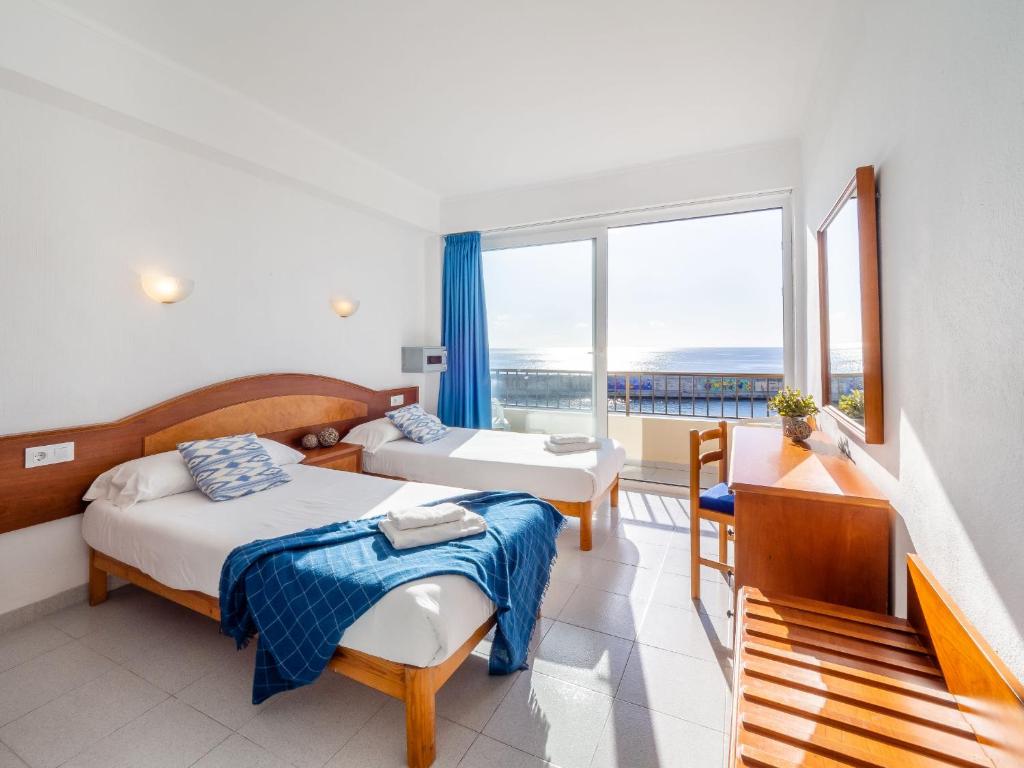 a hotel room with a bed, chair, and table at Hostal Port Corona in Cala Ratjada