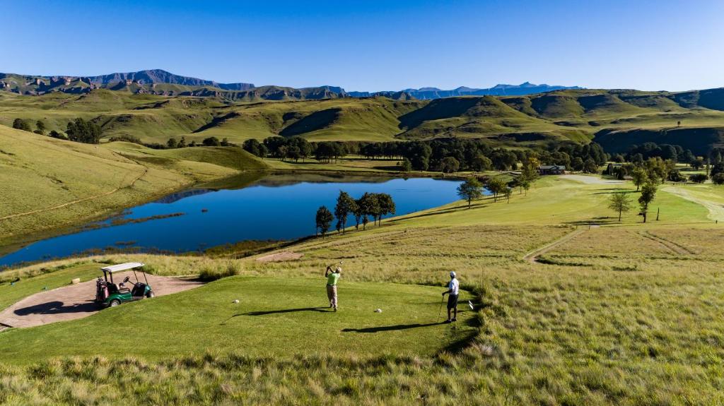 twee mensen die golfen op een golfbaan met een meer bij Gooderson Drakensberg Gardens Golf & Spa Resort in Drakensberg Garden