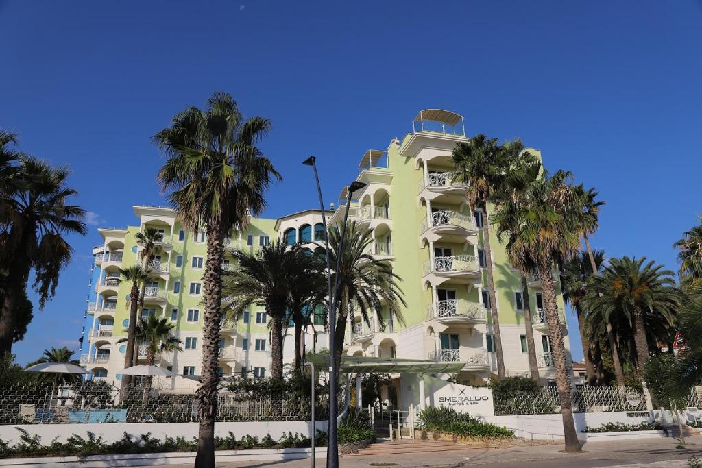 een geel gebouw met palmbomen ervoor bij Smeraldo Suites & Spa in San Benedetto del Tronto