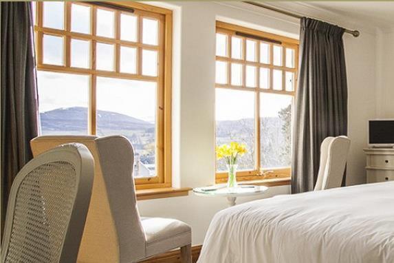 a bedroom with a bed and a table and windows at Sutherlands Guest House in Kingussie