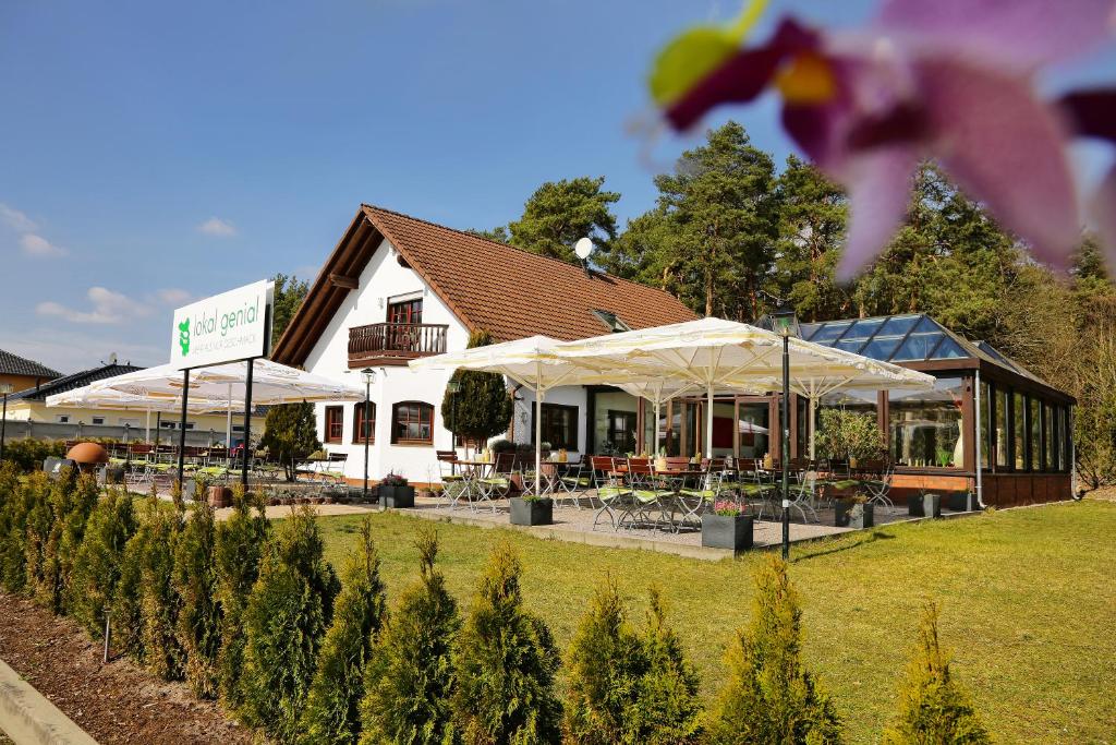 a building with white umbrellas in a yard with trees at Lokal Genial Pension & Restaurant in Beelitz