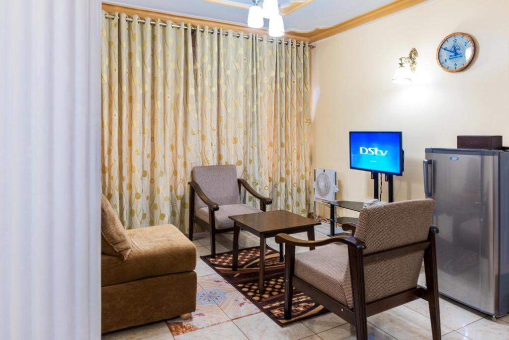 uma sala de espera com uma televisão e um sofá e cadeiras em Spacious apartment for 46 People in Kampala em Kampala