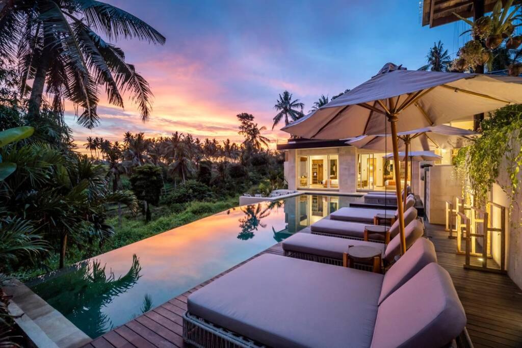 een huis met een zwembad met ligstoelen en een parasol bij Villa White Lotus by BaliSuperHost in Ubud