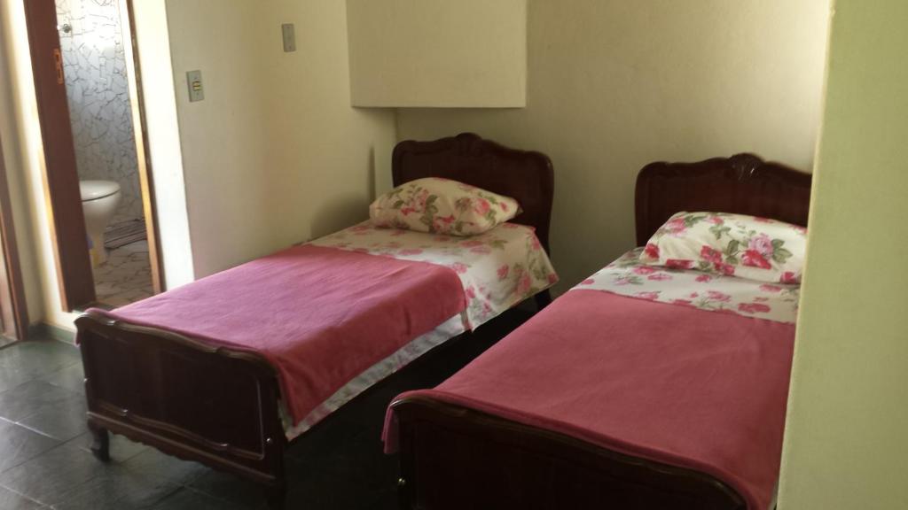 two beds in a small room with pink sheets at Pousada Chico Taquara in São Thomé das Letras