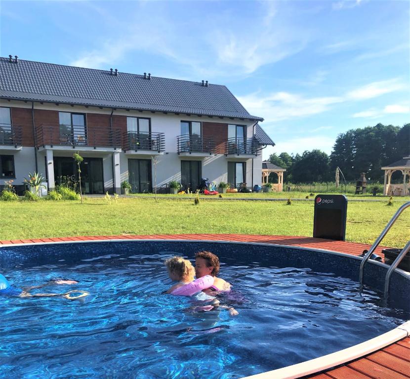two people in a swimming pool with a house in the background at Pokoje Gościnne Kameralnie in Jantar