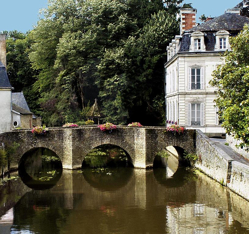 a stone bridge over a river in front of a building at La Demeure de l'Ile in Craon