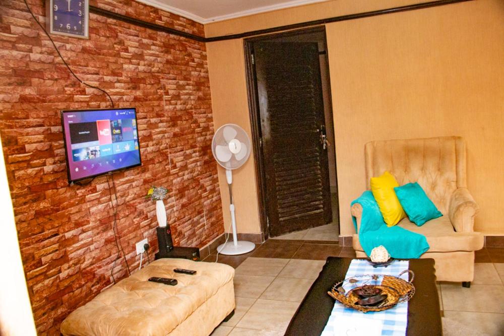 a living room with a couch and a tv on a brick wall at The White Dove - in Milimani Kisumu in Kisumu