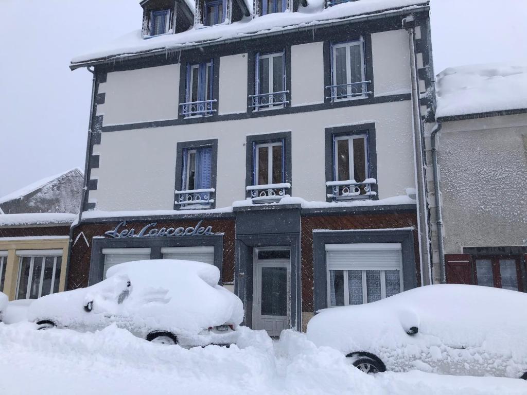 a building covered in snow with parked cars in front at Les cascades in Le Mont-Dore