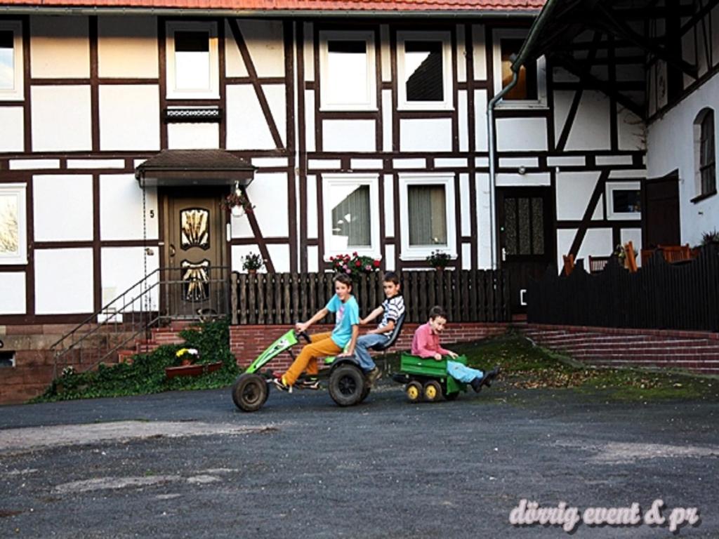 dos niños montados en coches de juguete delante de una casa en Anitas Landerlebnis en Witzenhausen