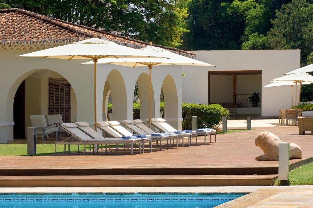 een groep ligstoelen met parasols naast een zwembad bij Garden Hill Hotel e Golfe in São João del Rei