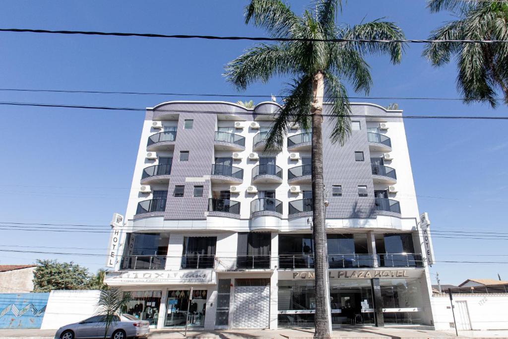 a tall white building with a palm tree in front of it at Pontal Plaza Hotel in Curvelo