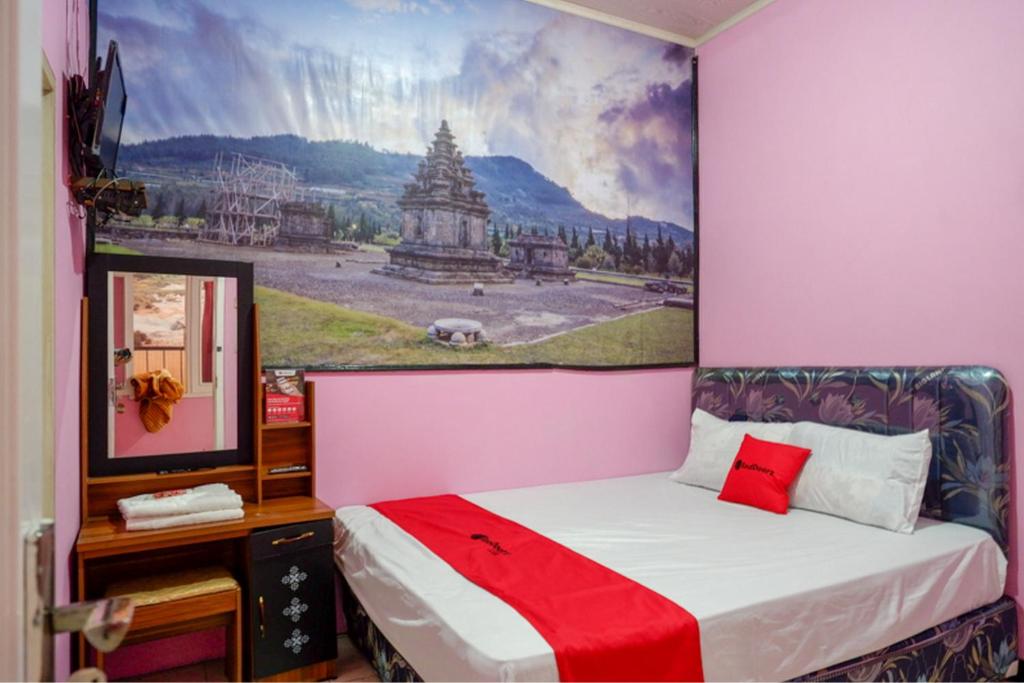 a pink room with a bed with a painting on the wall at RedDoorz Syariah near Telaga Warna Dieng in Diyeng