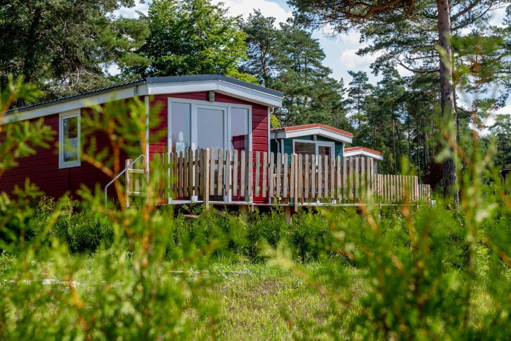 una casa roja con una valla en el césped en Naturcamping Lüneburger Heide - Chalets & Tiny Häuser en Soltau