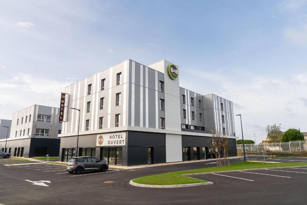 un grand bâtiment blanc avec une voiture garée dans un parking dans l'établissement B&B HOTEL Poitiers Aéroport, à Poitiers