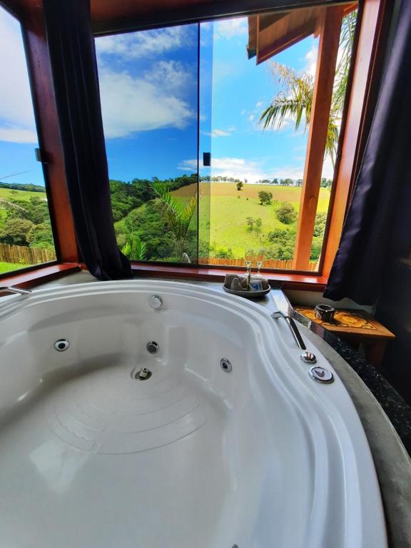 uma banheira num quarto com uma grande janela em Chalés e Bangalôs Capim Limão em Bueno Brandão