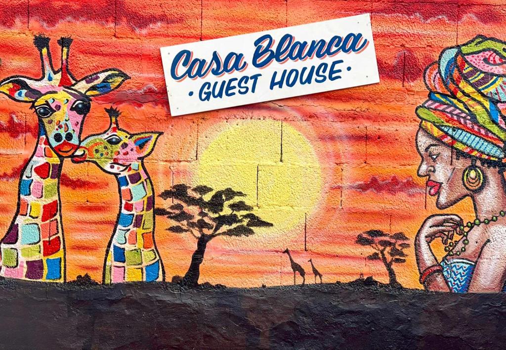 ein Bild von Giraffen an einer Wand mit einem Schild in der Unterkunft Casa Blanca Guest House Tenerife in Granadilla de Abona