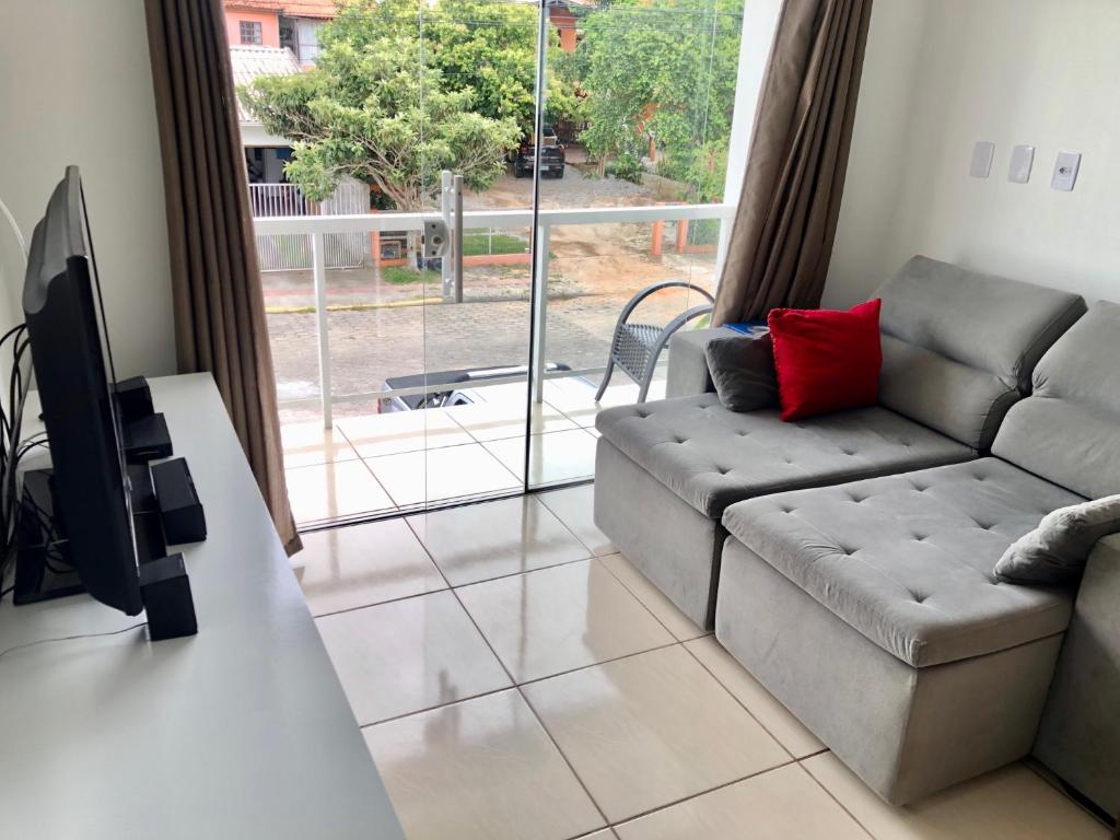 a living room with a couch and a large window at Residencial Sandini Garopaba in Garopaba