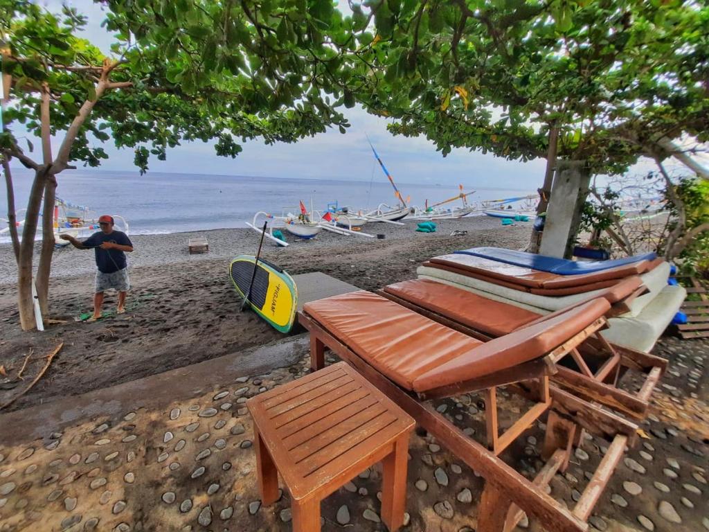 a man standing on a beach with a table and chairs at Solaluna Beach Homestay in Amed