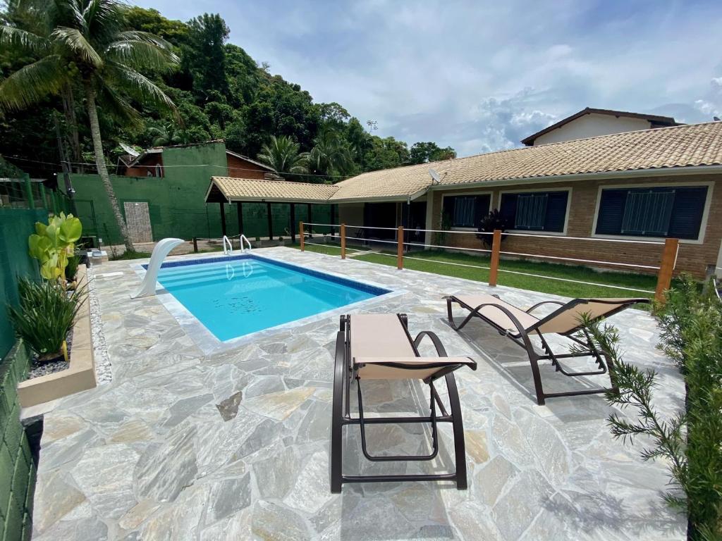 uma piscina com duas cadeiras ao lado de uma casa em Ampla casa com piscina a 200 metros da praia do Lazaro e Sununga em Ubatuba