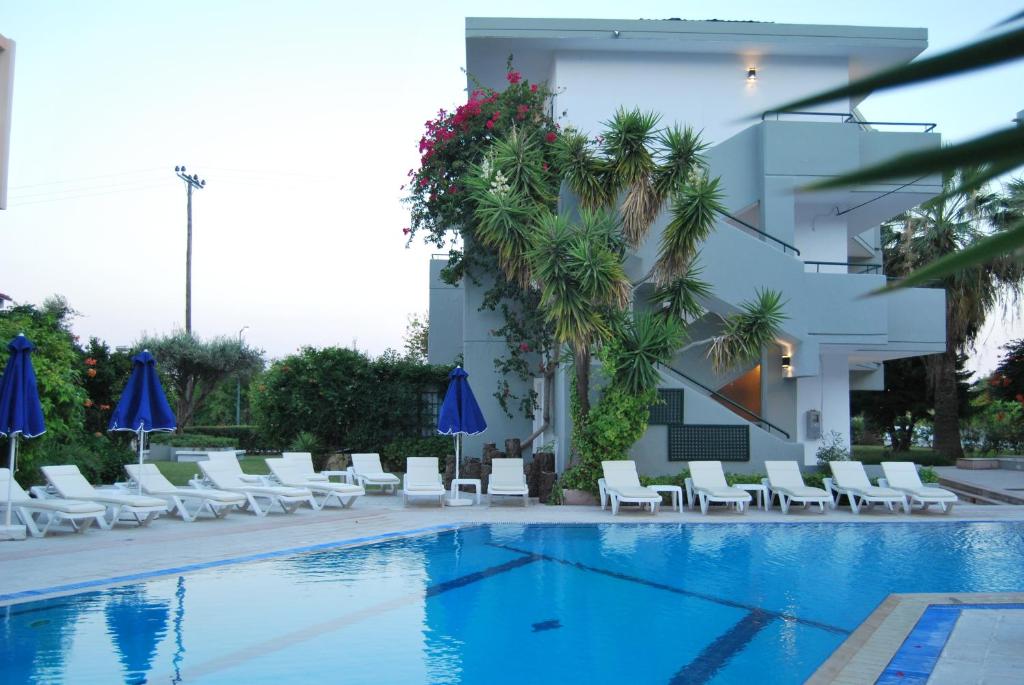 a hotel swimming pool with white chairs and blue umbrellas at Artemis Studios in Faliraki