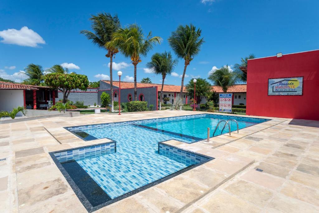 a swimming pool with palm trees and a red building at OYO Pousada Horizonte in Horizonte