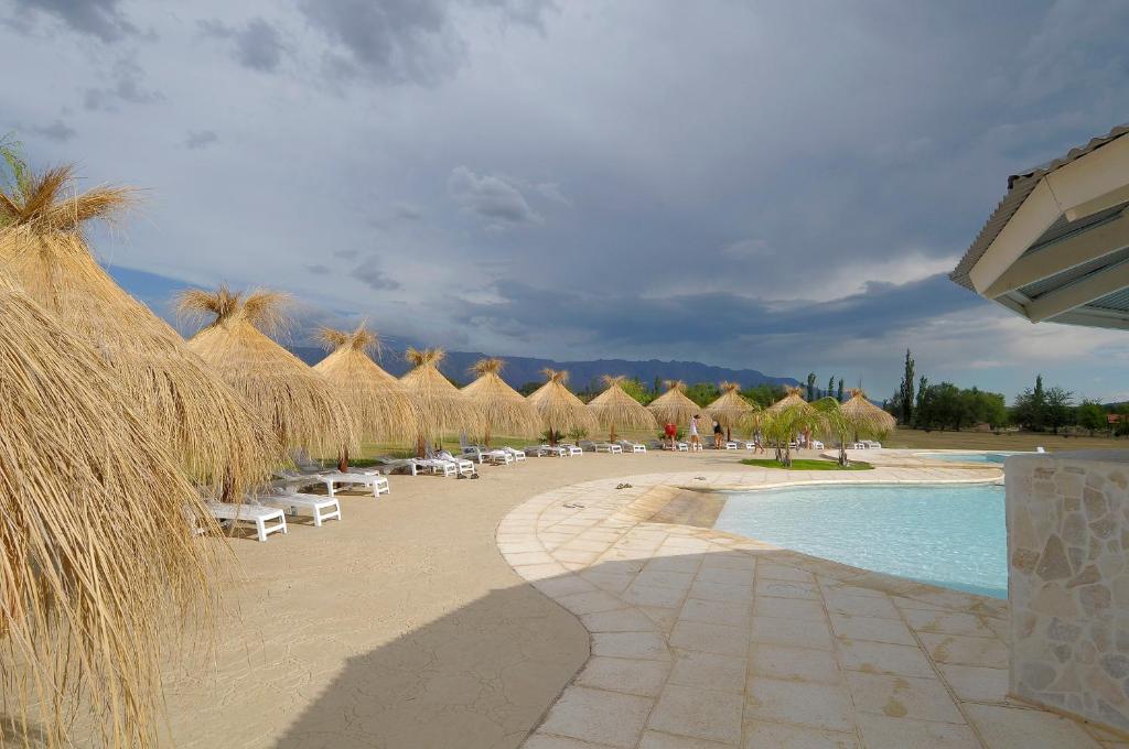 una playa con sombrillas y sillas de paja y una piscina en Arenas Blancas Cabañas & Suites en Nono