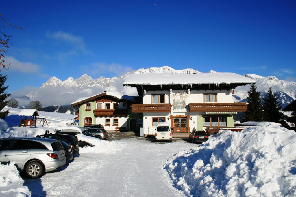 ein schneebedecktes Haus mit Autos auf einem Parkplatz in der Unterkunft Wellness-Pension Jagahütt'n in Schladming