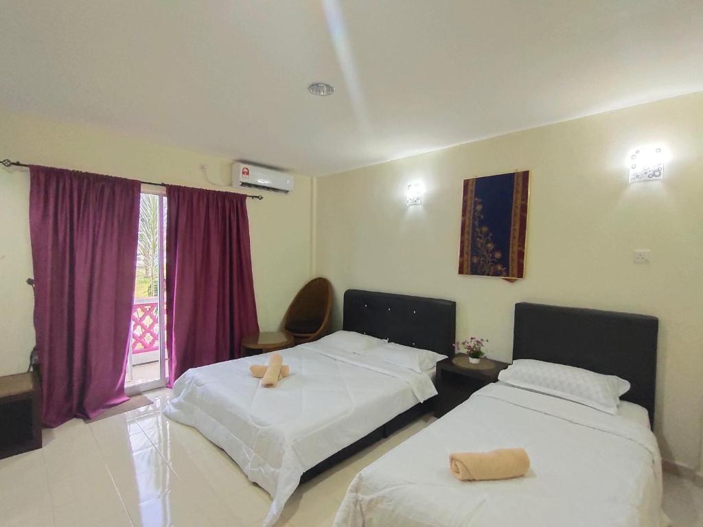 a bedroom with two beds and a window with purple curtains at Huda Inn in Pantai Cenang