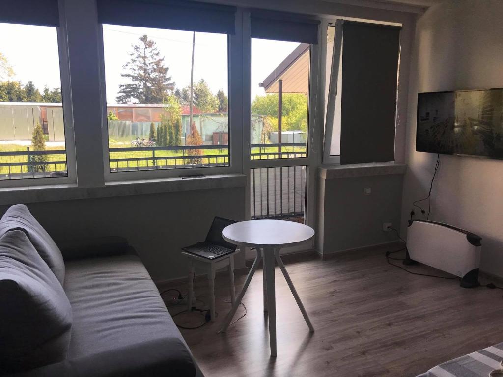 sala de estar con sofá, mesa y ventanas en Apartament Leśna Jarosławiec, en Jarosławiec