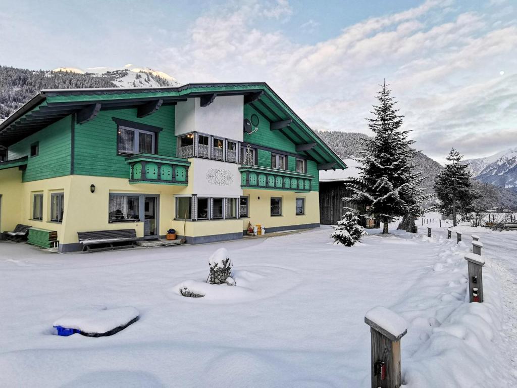 a green and yellow building in the snow at Appartment Sonnenkogel in Holzgau