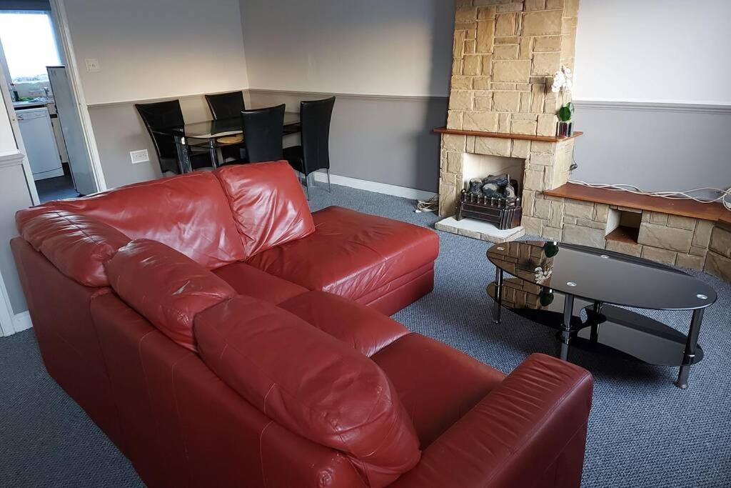 a living room with a red leather couch and a fireplace at Wonderland Guest House in Coventry