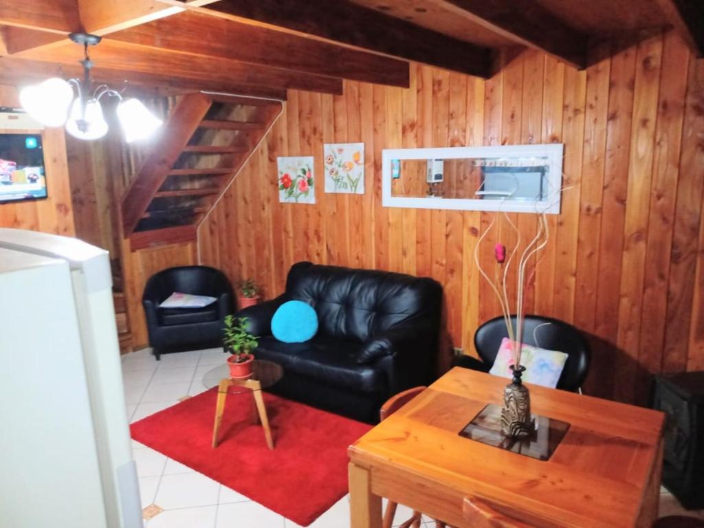 a living room with a black leather couch and a table at CABAÑA INTERIOR VILLARRICA in Villarrica