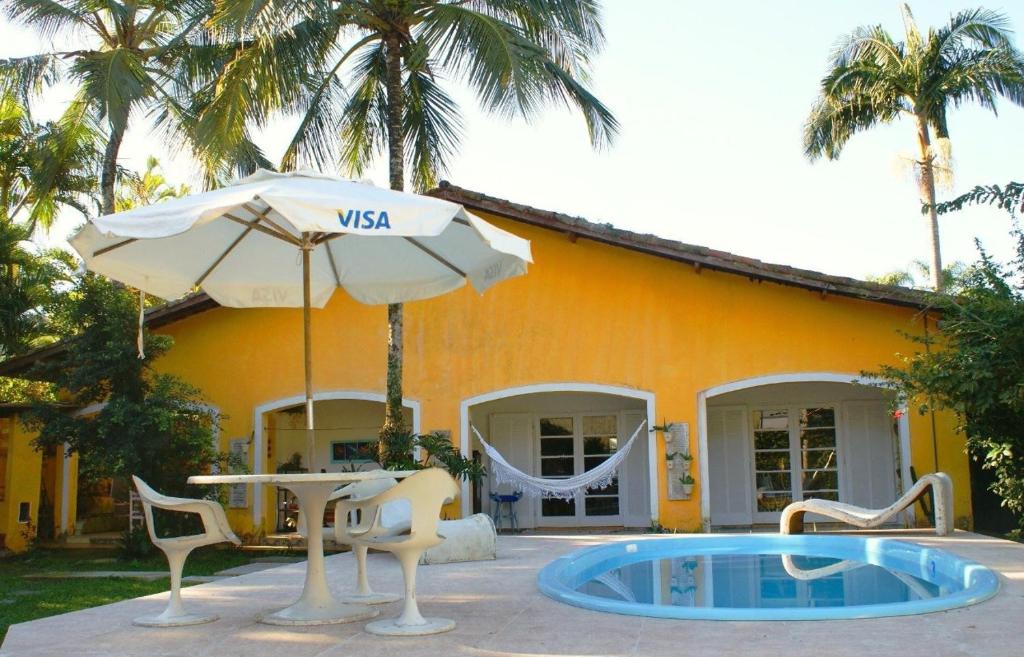 a house with a table and an umbrella and a pool at Casa pé na areia in Guarujá